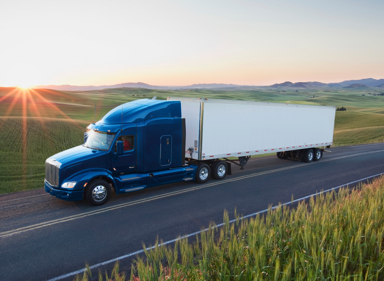 An 18-wheeler truck cruising down a highway with a radiant sunset in the background, symbolizing traceability, efficiency, and scenic journeys.